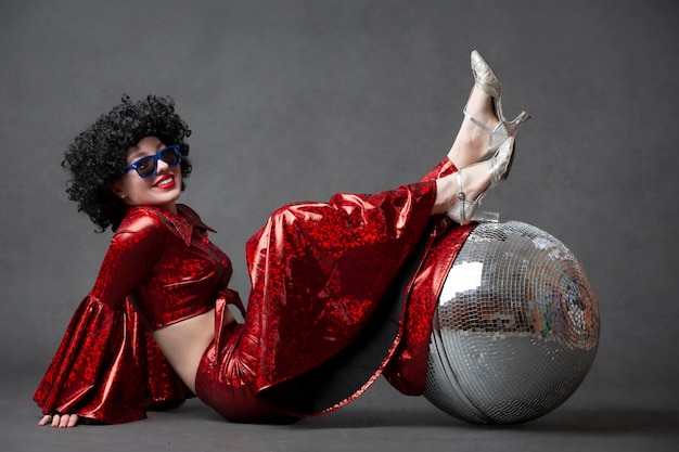 Woman in a wig with a disco ball on a gray backgroundGirl in disco style on a gray background