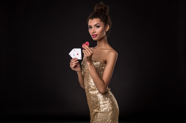 Woman winning - Young woman in a classy gold dress holding two aces and two red chips, a poker of aces card combination.