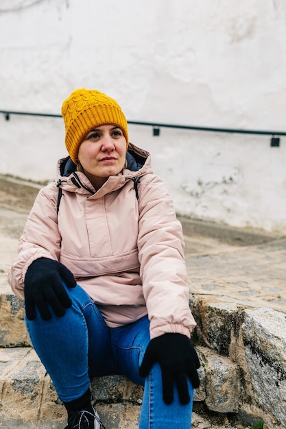 Woman in winter clothes sitting on the stairs by the white wall