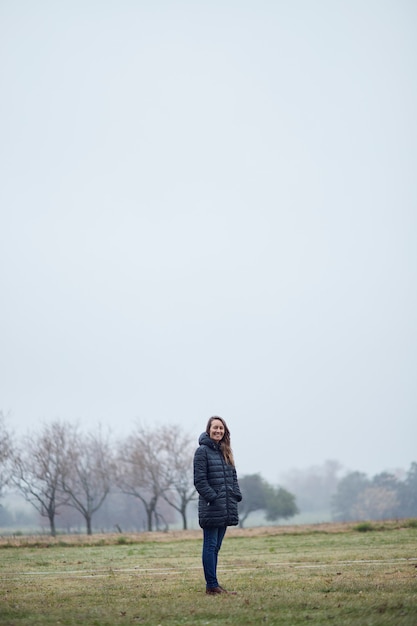 Woman in winter coat standing in the field, among the mist.