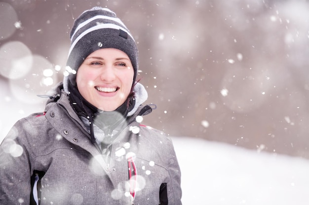 冬の季節の女性冬の森で彼女の周りに雪片と雪の日を楽しんでいる暖かい服を着た若い女性の肖像画