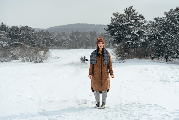 雪の降る冬の森を歩く冬の暖かいジャケットの女性