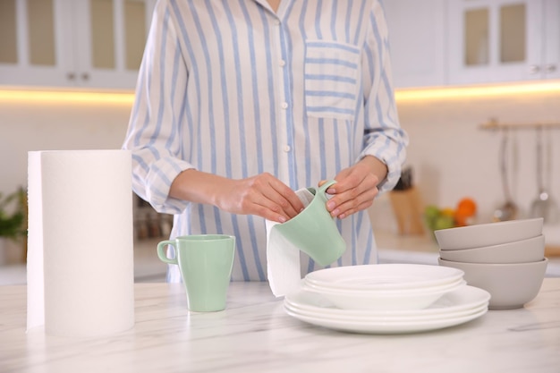 キッチンのクローズ アップでペーパー タオルでカップを拭く女性