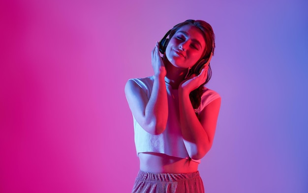ネオンの光の下で目を閉じてリラックスしてお気に入りの曲を聴いているワイヤレスヘッドフォンの女性
