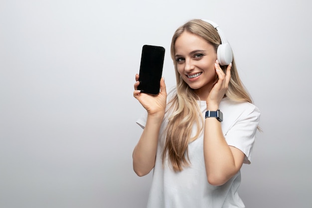 Woman in wireless headphones with vertically positioned blank screen on phone with mockup isolated