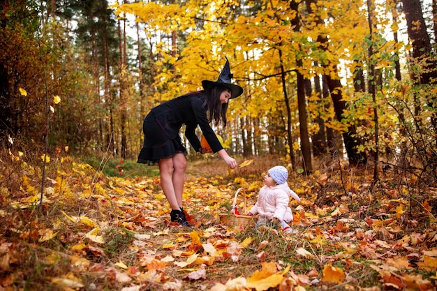 女性の魔女は、秋の森のハロウィーンのコンセプト衣装の魔女とウサギの小さな子供と遊ぶ