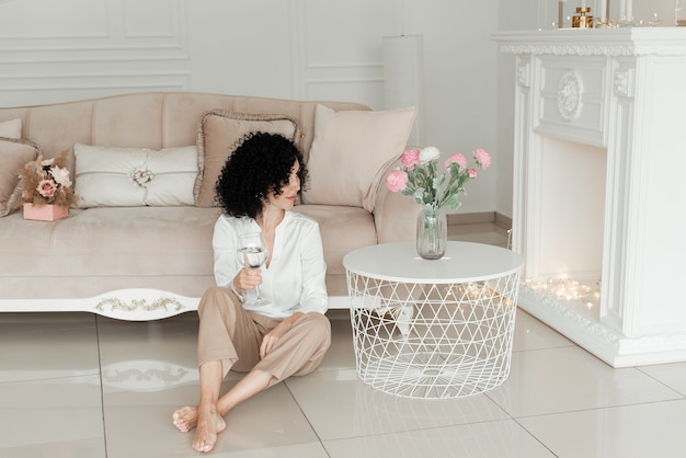 Woman with African curls sits on the floor with a glass in her hand