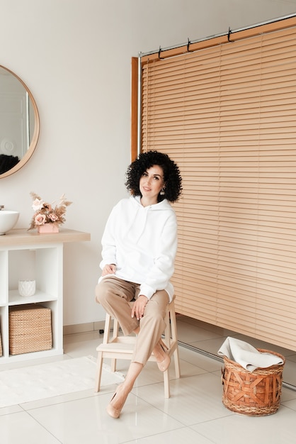 Woman with african curls in a white sweater smiles and sits on a chair