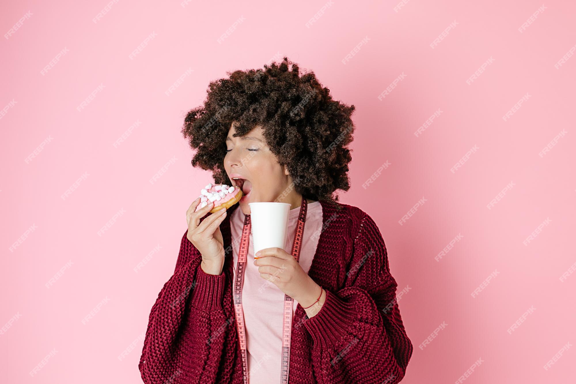 Premium Photo | Woman with afro hairstyle holds donut, biting it, enjoy hot drink of coffee or tea in paper cup in her hands. tape for measurement hangs around neck Premium Photo | Woman with afro hairstyle holds donut, biting it, enjoy hot drink of coffee or tea in paper cup in her hands. tape for measurement hangs around neck