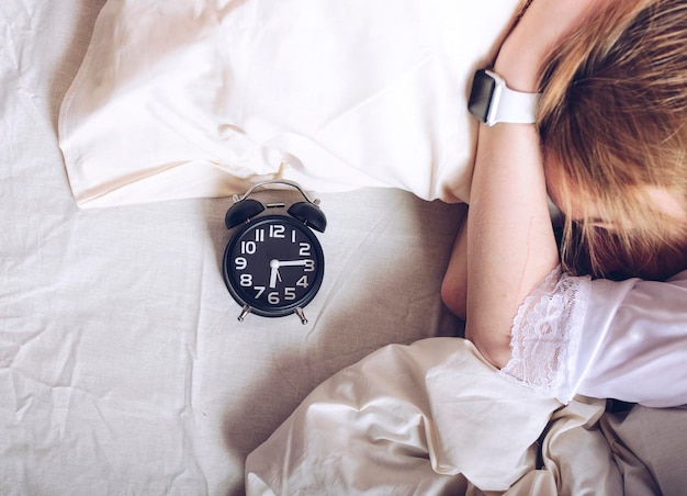 Photo woman with alarm clock sleeping on bed at home