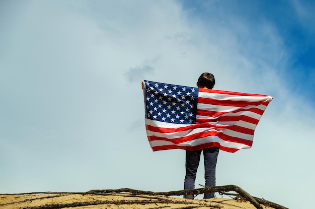 Woman with an American flag stands on the sand skies on the background Woman is holding with both hands waving American USA flag Fourth of July Independence Day