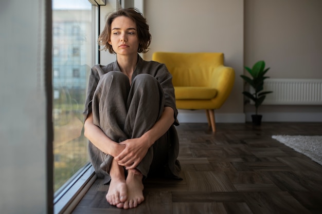 Woman with anxiety sitting on floor full shot