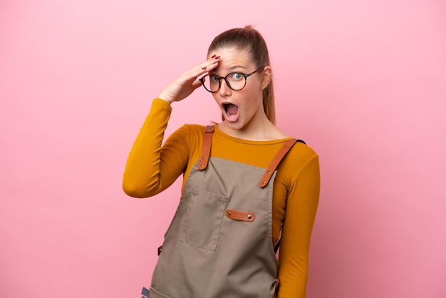 Woman with apron isolated on pink background doing surprise gesture while looking to the side