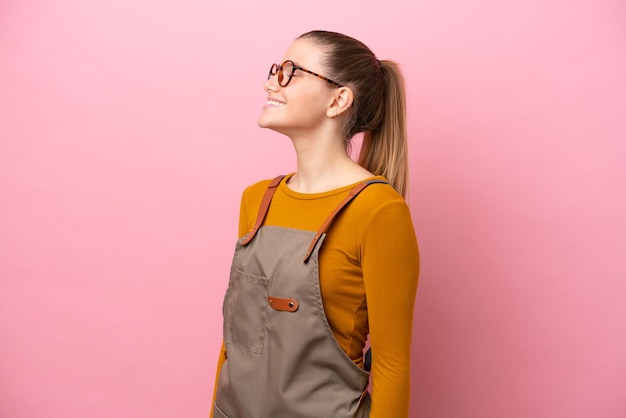 Woman with apron isolated on pink background laughing in lateral position