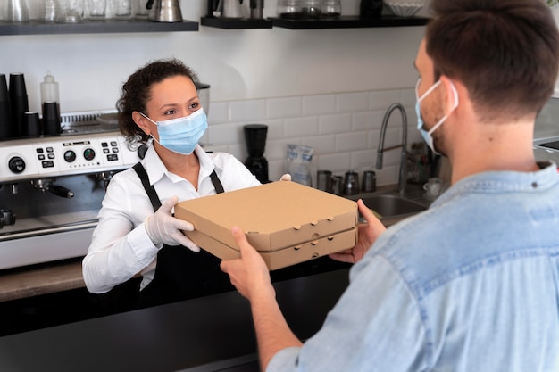 Photo woman with apron offering packed takeaway food to male customer