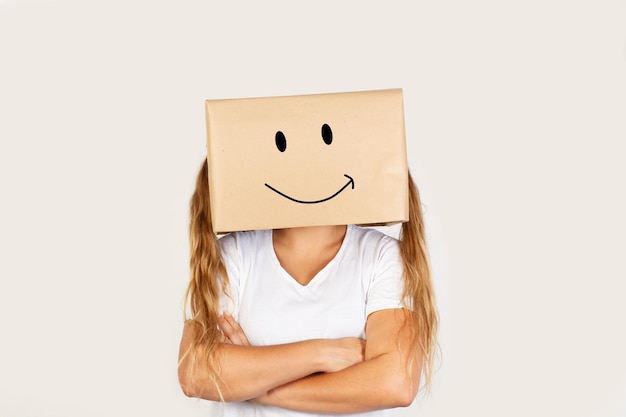 Woman with arms crossed and her head in a box and smily gesture drawn on it on a white background