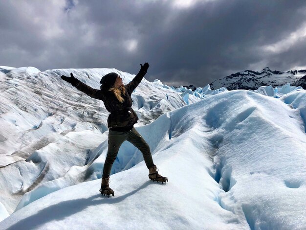 写真 雪で覆われた山に背を向けて腕を伸ばした女性