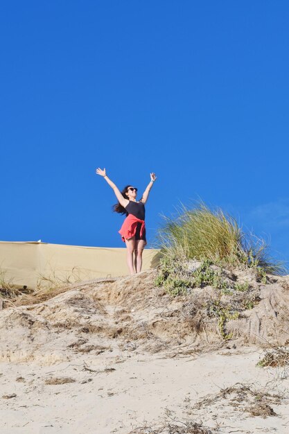 Foto donna con le braccia alzate sulla spiaggia contro un cielo limpido