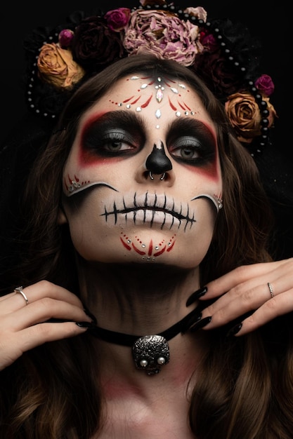 Женщина с художественным жутким макияжем и свежими цветами на голове стоит, готовясь к вечеринке в честь хэллоуина