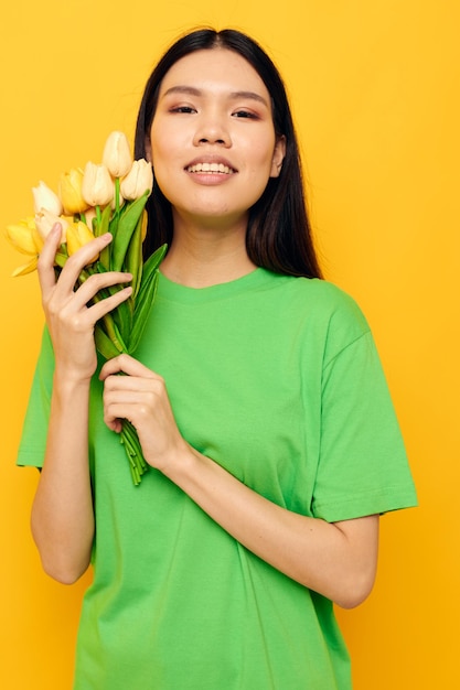 Woman with Asian appearance green tshirt a bouquet of yellow flowers yellow background unaltered