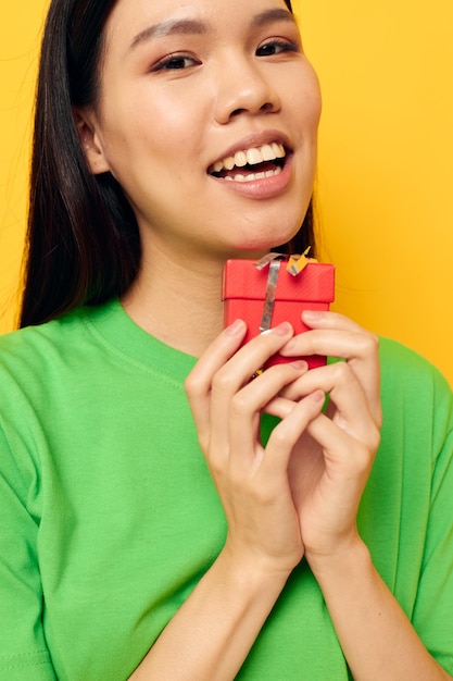 Woman with asian appearance in green tshirts with a small gift box yellow background unaltered