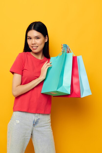 赤いTシャツのアジアの外観のショッピングバッグの女性は、変更されていない背景を分離しました