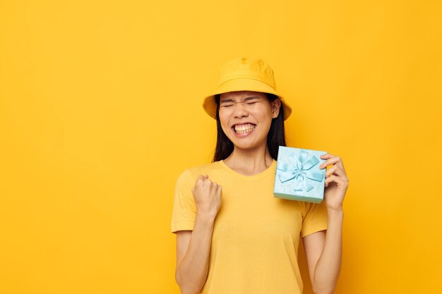 Woman with Asian appearance in a yellow Tshirt and a hat with a gift studio model unaltered