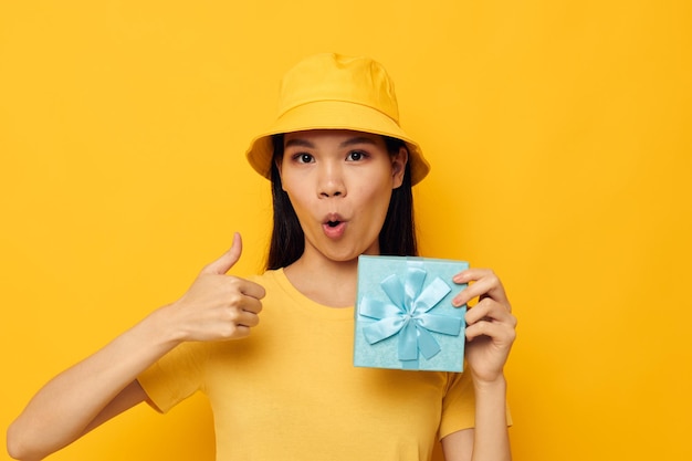 Woman with Asian appearance in a yellow Tshirt and a hat with a gift studio model unaltered