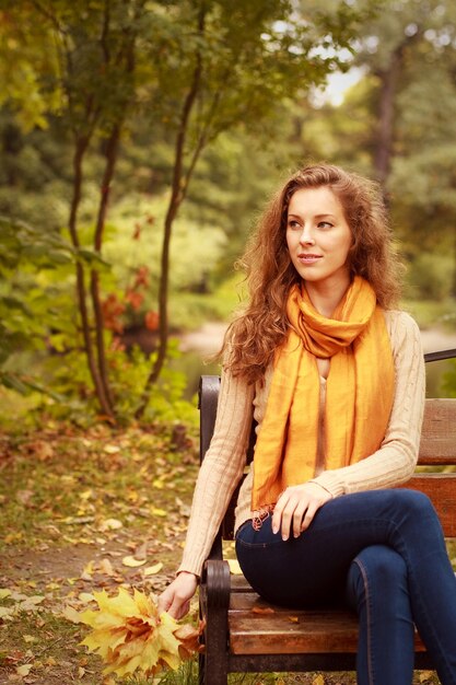 Woman with autumn leaves sitting on bench