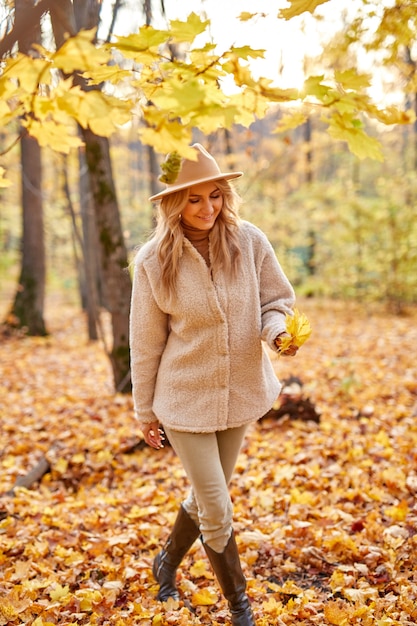 Donna con foglie di autunno nella natura soleggiata, parco o foresta