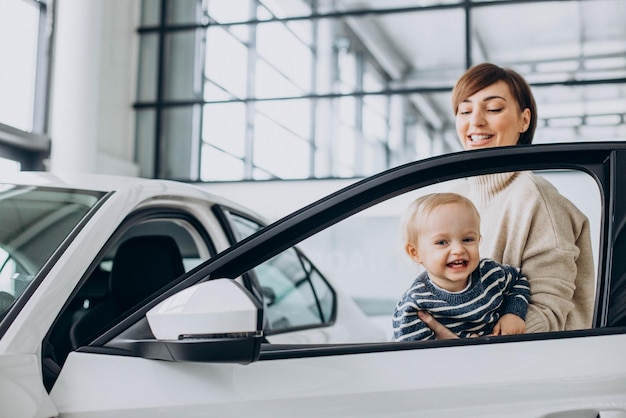 Woman with baby son choosing a car in a car salon