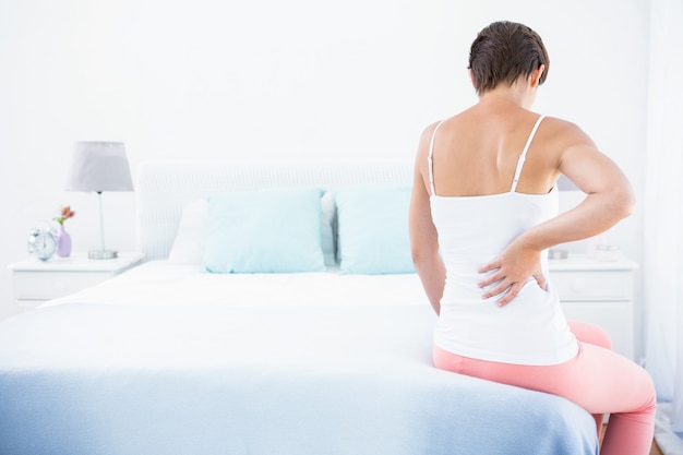 Woman with back pain at home in the bedroom 