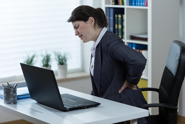 A woman with a back pain sits at a desk in an office.