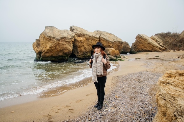 美しい海に対して岩の背景に海岸のバックパックを持つ女性