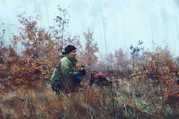 woman with backpack having break during autumn trip drinking a hot drink from thermos flask