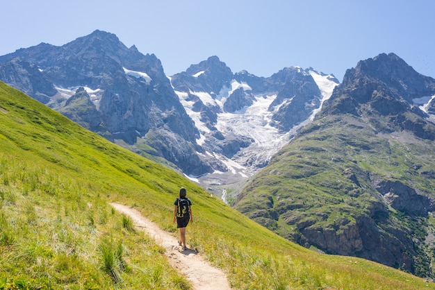 Woman with backpack hiking on mountain, scenic glacier and dramatic landscape summer fitness wellbeing rear view, freedom concept