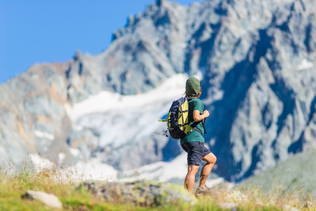 Woman with backpack hiking on mountain, scenic glacier and dramatic landscape summer fitness wellbeing rear view, freedom concept