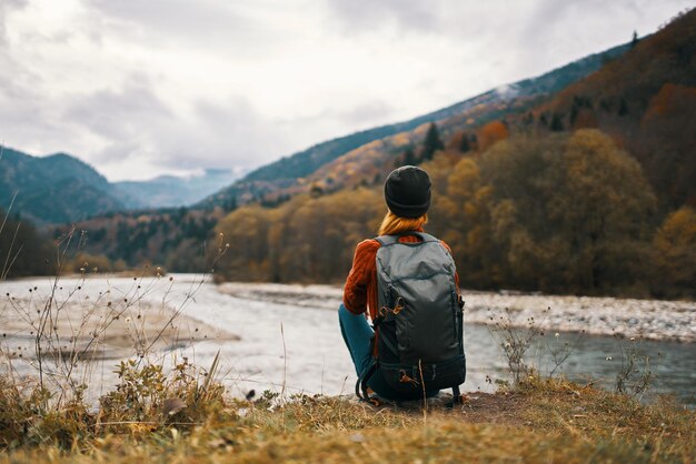 Foto la donna con lo zaino sulla sponda del fiume ammira il paesaggio della montagna nei precedenti