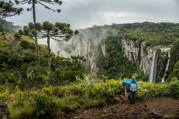 Woman with a backpack standing on the edge of a cliff and looking at the waterfall