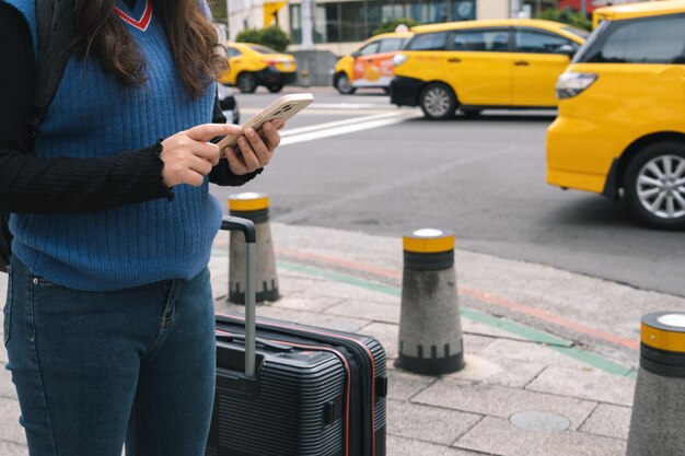 Женщина с багажем на улице в центре города заказывает такси с помощью приложения для смартфона Бронирование такси с помощью онлайн-приложения на смартфоне
