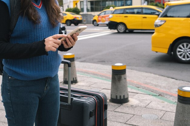 Woman with baggage in downtown city street ordering taxi using smart phone app Booking taxi using application online on smart phone