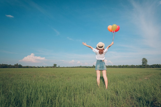 Woman with balloons standing on field against sky