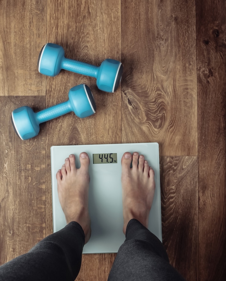 Photo woman with bare feet is weighed on the scales on the floor with dumbbells.. fitness concept