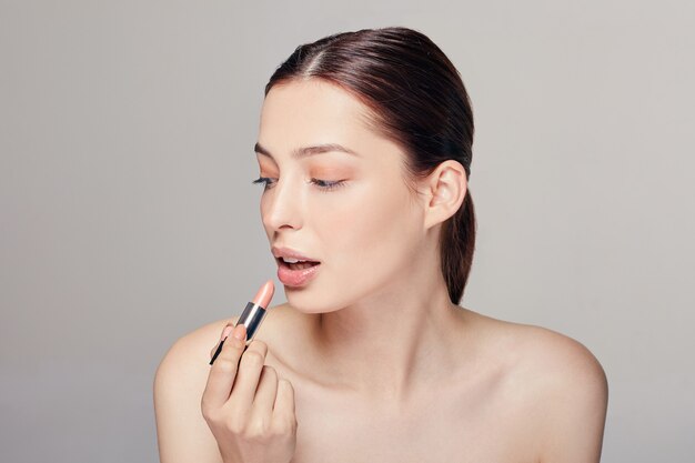 woman with bare shoulders with lipstick in her right hand paints chubby lips