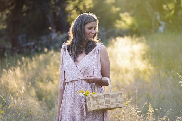 Woman with basket of flowers in a meadow at sunset