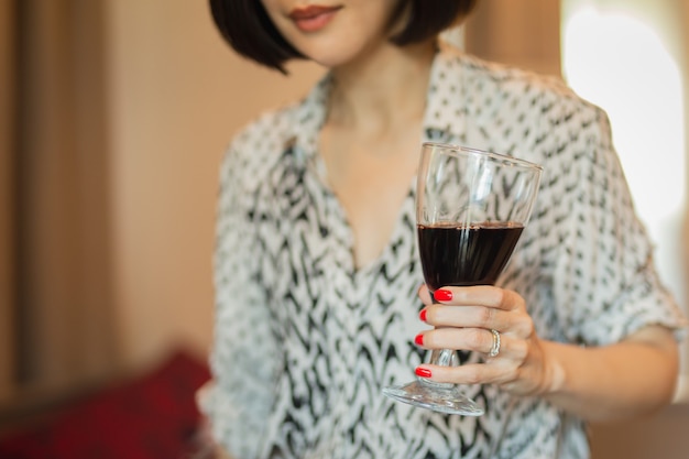 Woman with beautiful red manicure holding glass of red wine.