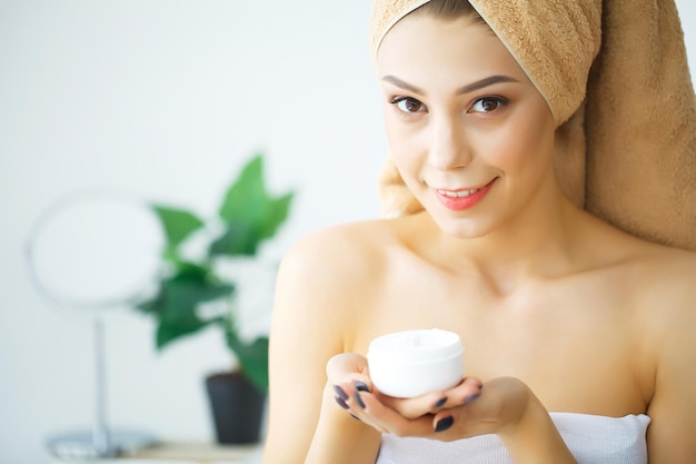 Woman with beautiful silky skin applies moisturizer on her face.