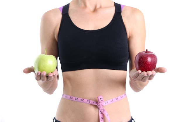 허리에 센티미터가 있는 아름다운 날씬한 몸매를 가진 여성은 두 개의 빨간색과 녹색 사과를 가지고 있습니다