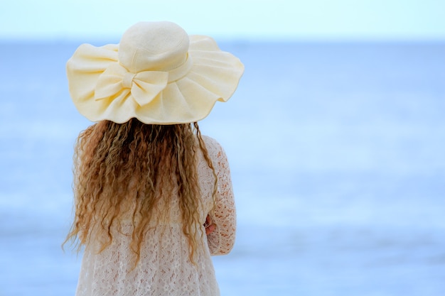 Woman with big hat looking to blue sea