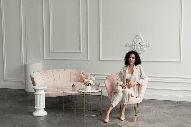 Woman with black curly hair sits in a pink armchair next to a bouquet